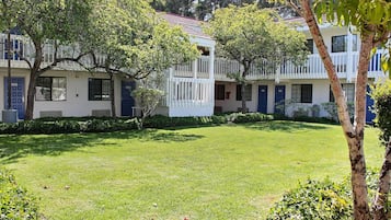 A courtyard with a grassy lawn, white buildings with balconies, and trees.