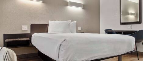A hotel room with a bed, bedside table, and a desk with a chair.