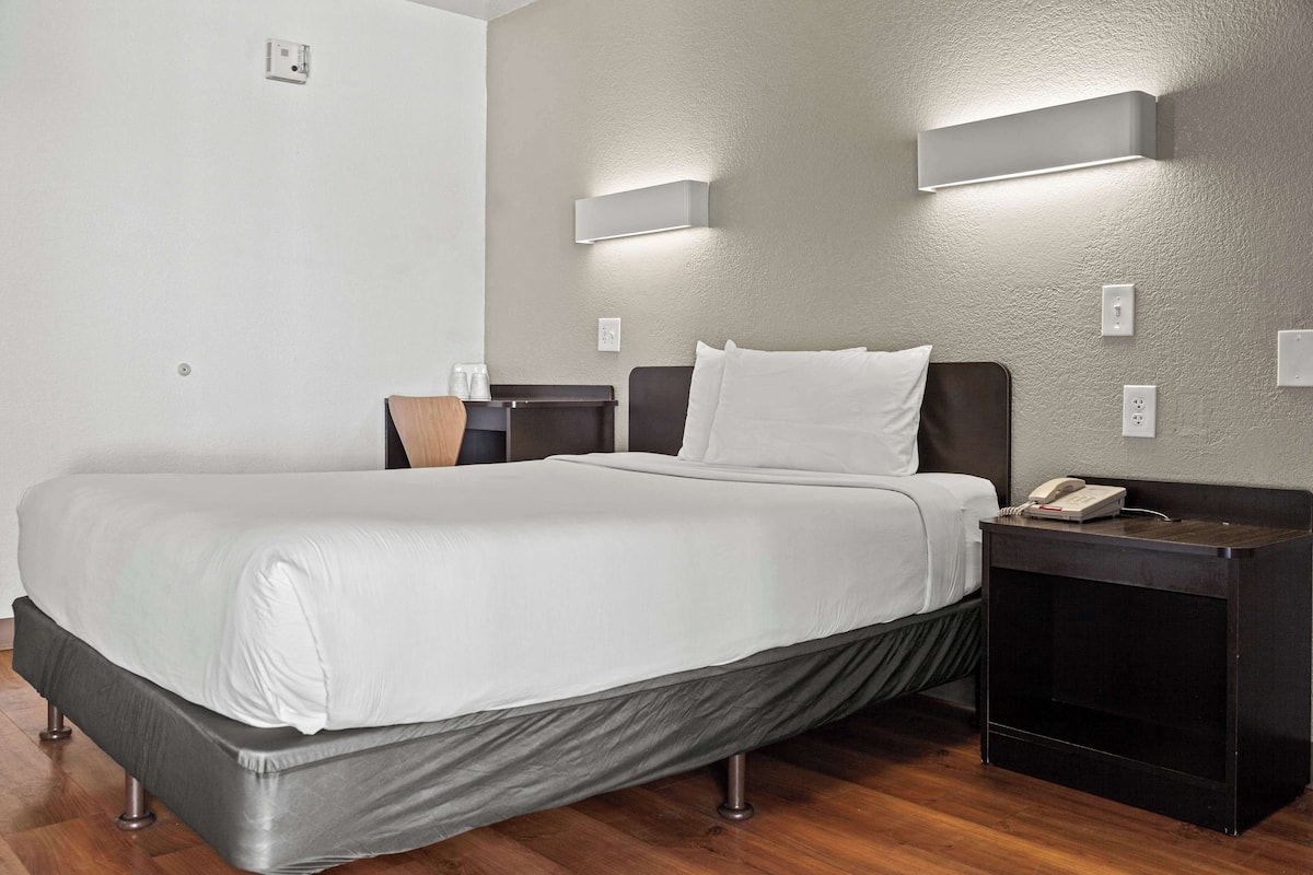 A hotel room with a bed, bedside tables, and wall-mounted lighting.