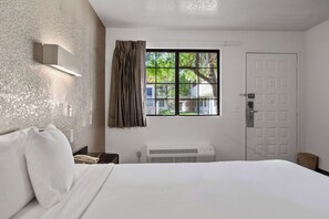 Una habitación de hotel con cama, ventana con cortinas, una lámpara de pared y una puerta.