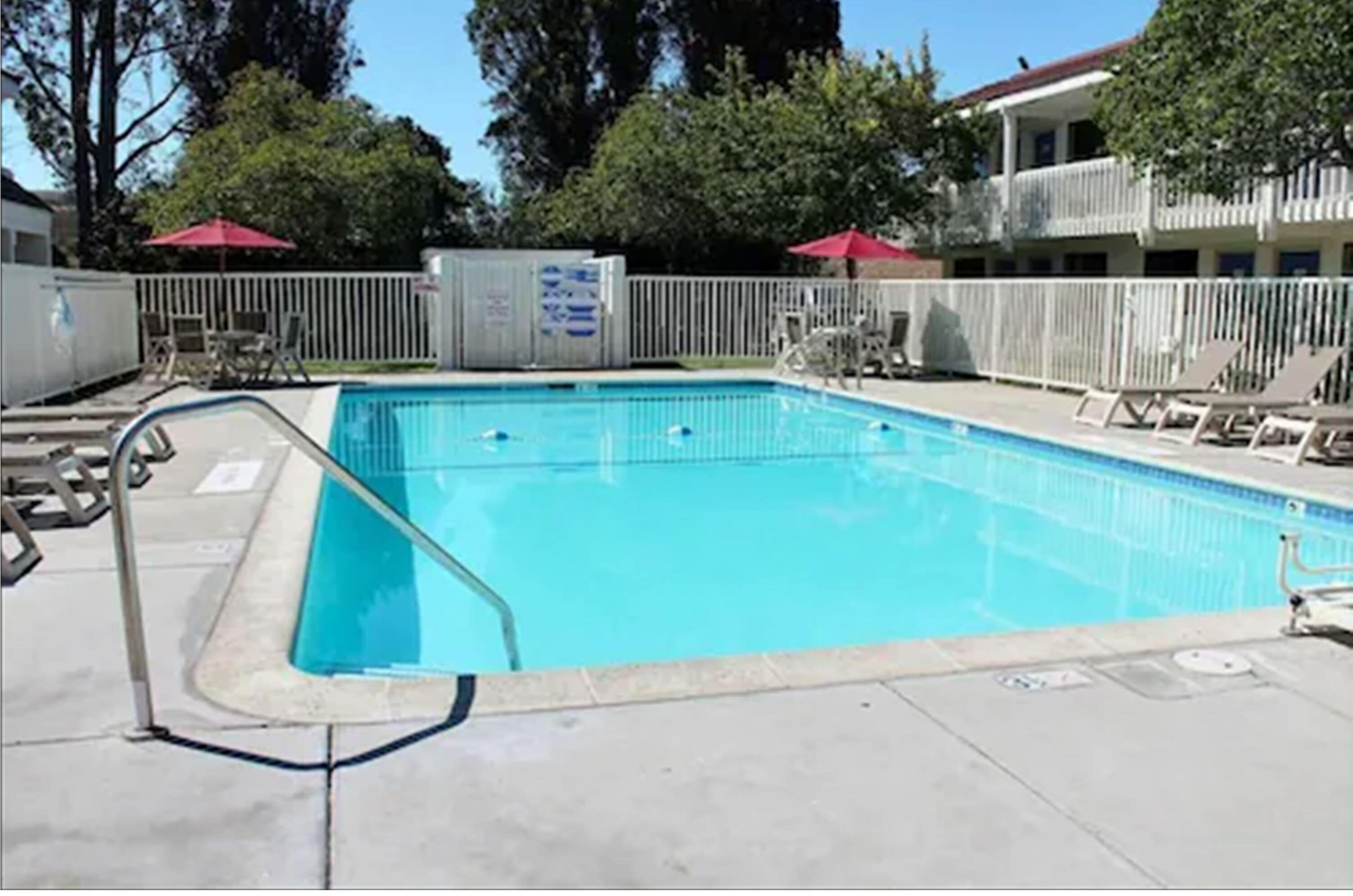 A rectangular swimming pool with a white deck and a metal ladder. There are lounge chairs and umbrellas around the pool.