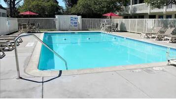 A rectangular swimming pool with a white deck and a metal ladder. There are lounge chairs and umbrellas around the pool.