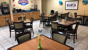 A breakfast area with tables and chairs, a coffee machine, and a clock on the wall. - Baymont by Wyndham Fort Wayne (Fort Wayne)