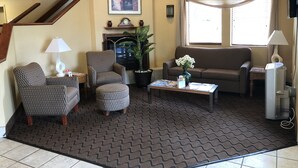 A living room with a patterned sofa, armchairs, a coffee table, a fireplace, a potted plant, and a large window with curtains. - Baymont by Wyndham Fort Wayne (Fort Wayne)