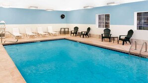 A swimming pool with lounge chairs and tables, a ceiling light fixture, and a window with a view. - Baymont by Wyndham Fort Wayne (Fort Wayne)