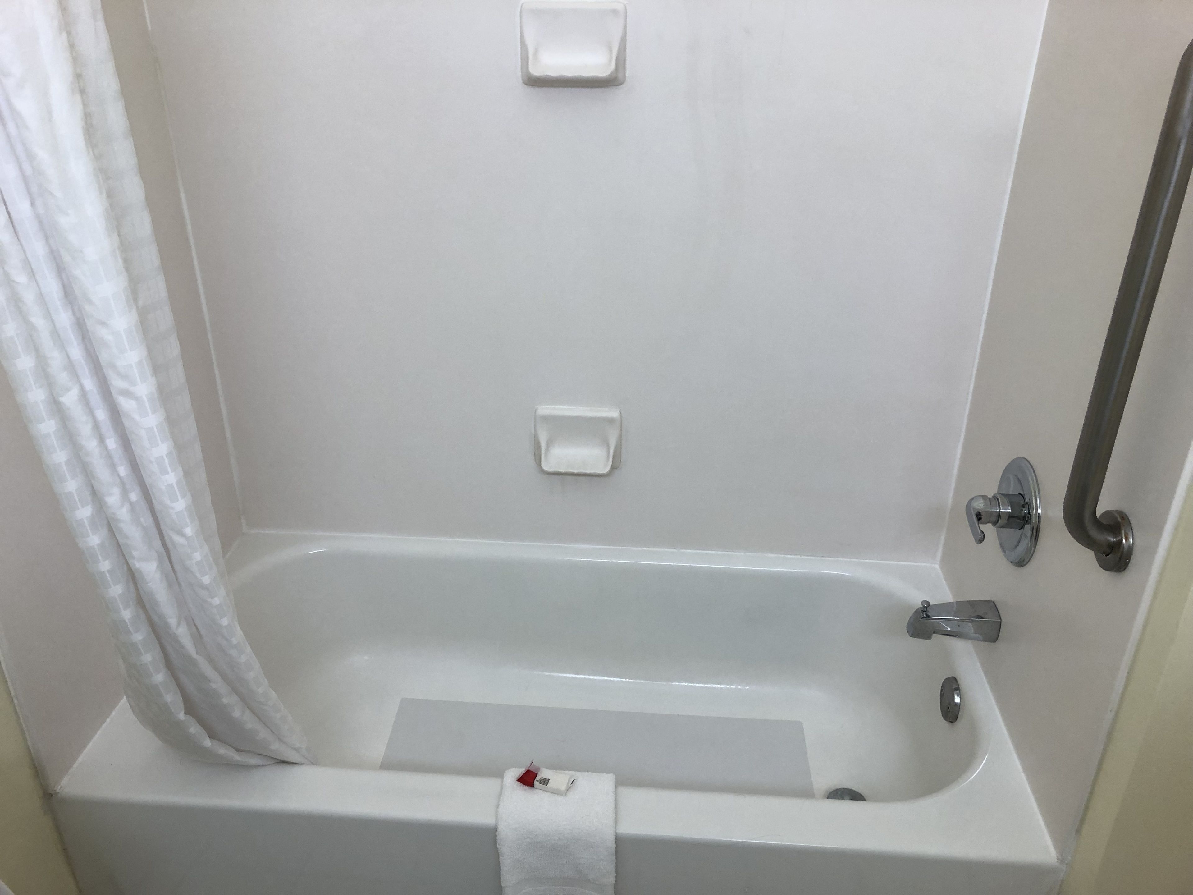 A white bathtub with a shower curtain, a soap dish, and a grab bar.