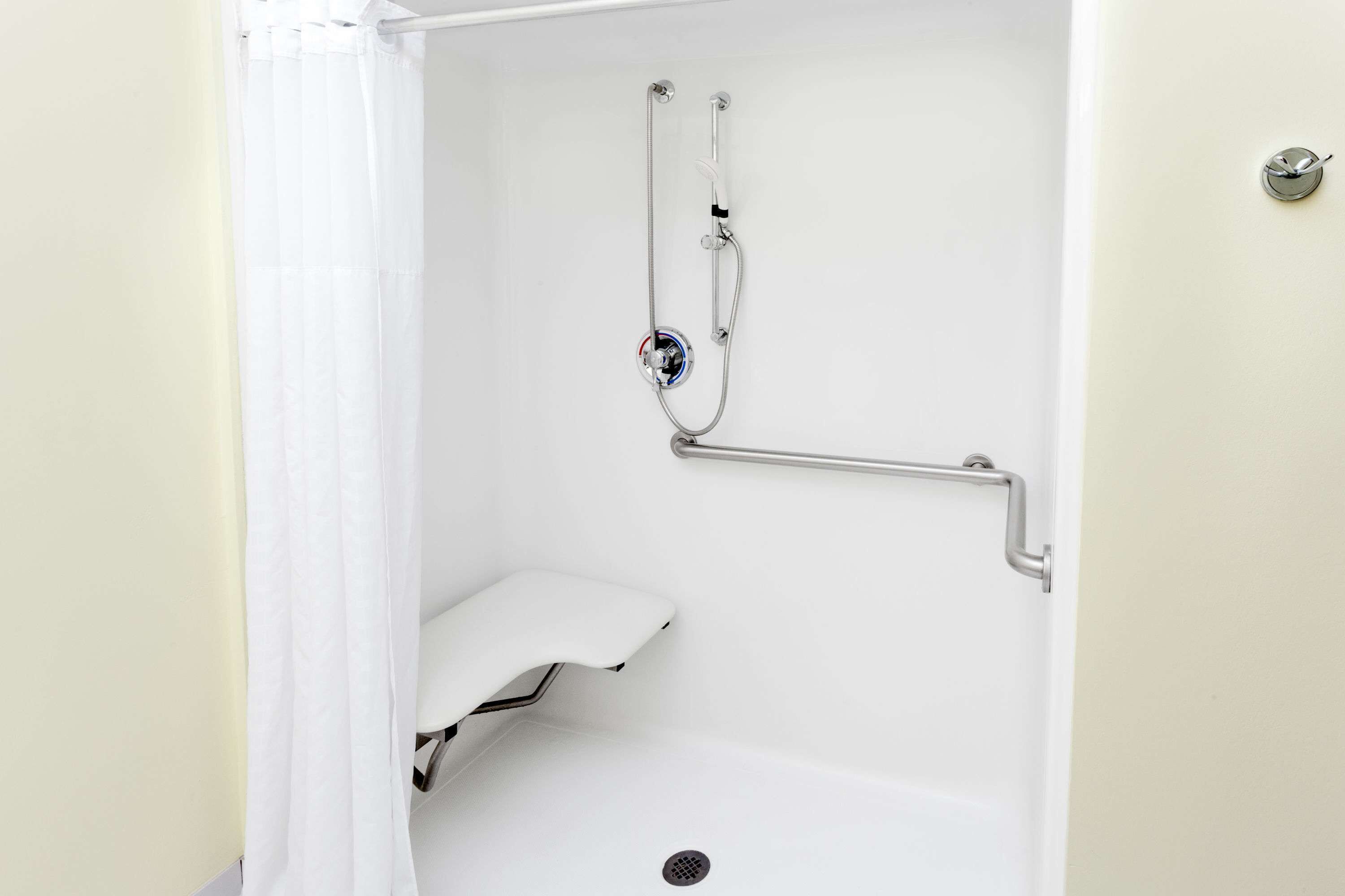 A white shower enclosure with a handheld showerhead, a grab bar, and a white seat.