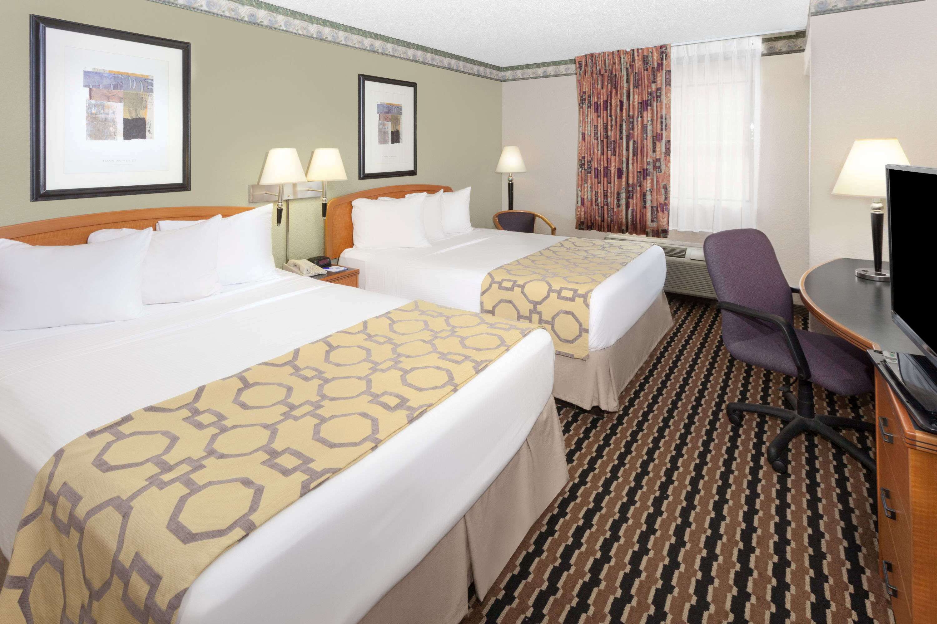 A hotel room with two beds, a desk, a chair, and a television.