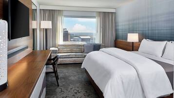 A hotel room with a bed, a desk, a TV, and a view of the city.