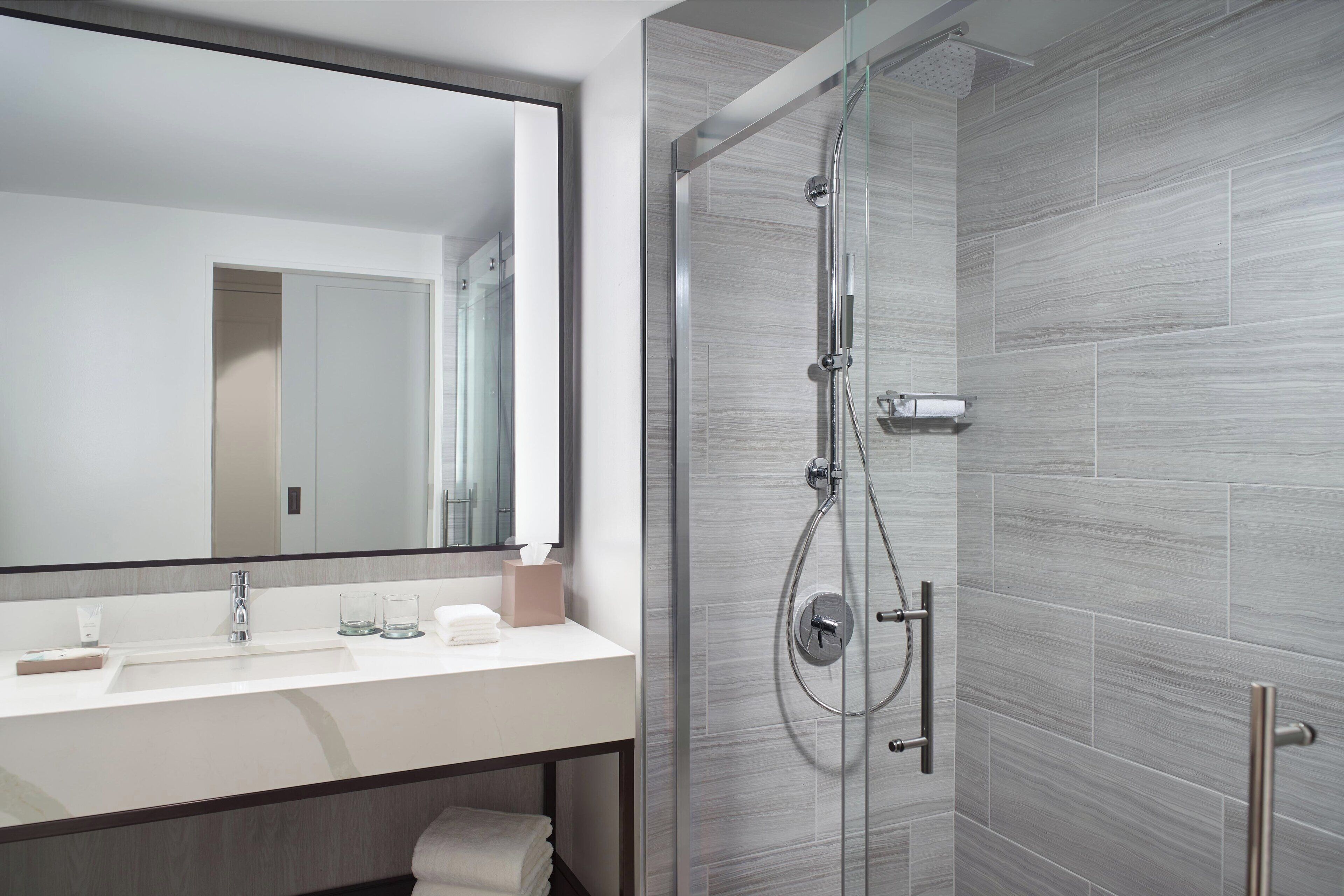 A modern bathroom with a glass-enclosed shower, a large mirror, and a white sink with a towel and glass.