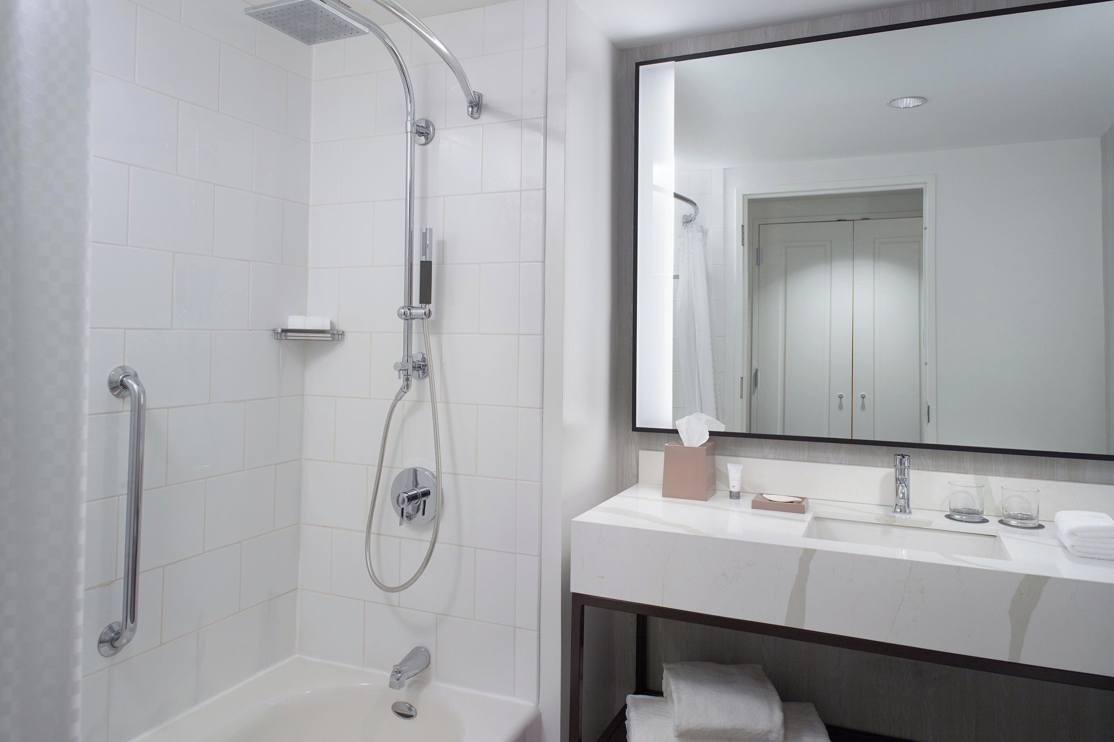 A modern bathroom with a walk-in shower, a bathtub, a large mirror, and a vanity with a sink and towel rack.