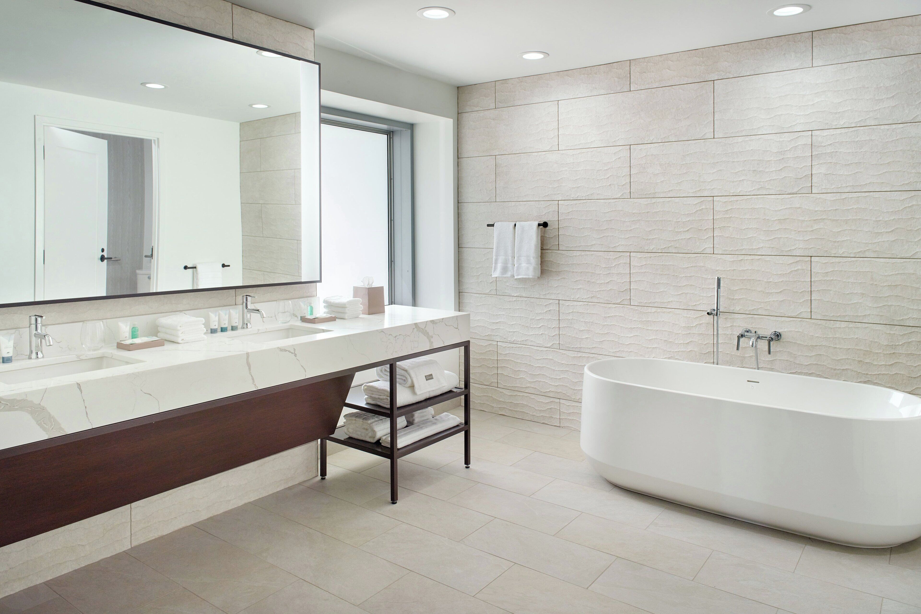 A modern bathroom with a large mirror, a bathtub, and a vanity with a dark wood cabinet.