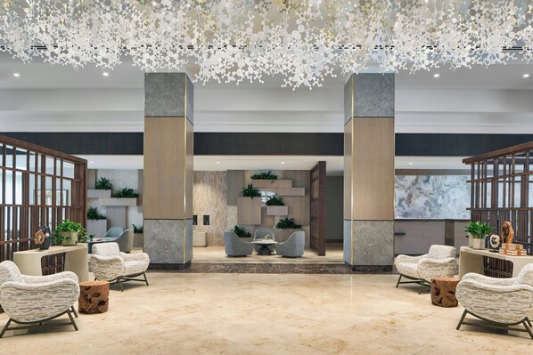 Um hall espaçoso com piso de mármore, dois pilares grandes e um lustre decorativo no teto.