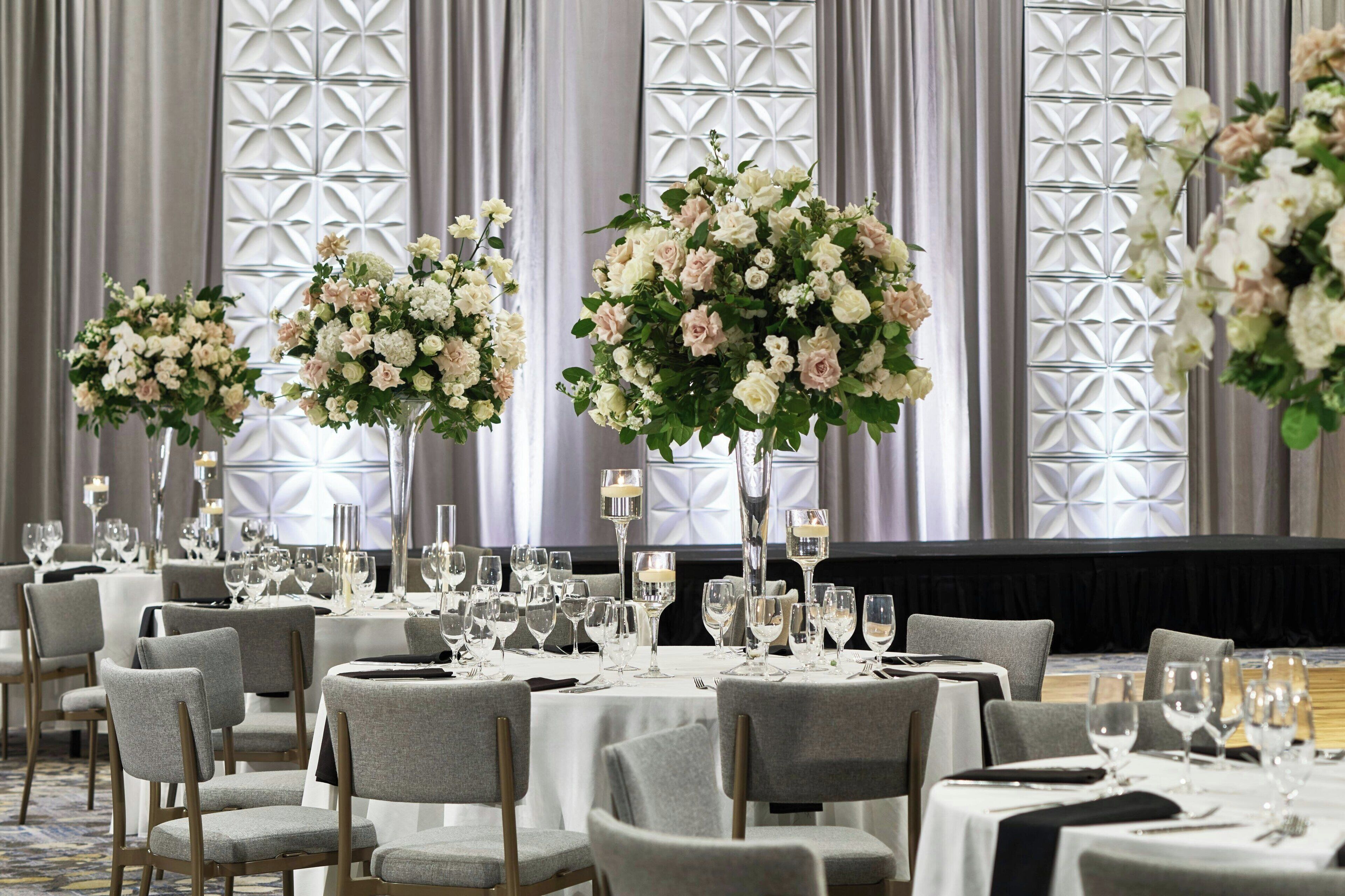 A banquet hall with round tables, grey upholstered chairs, and floral centerpieces.