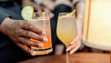 Un gros plan de deux mains tenant deux verres remplis de boissons, l’un contenant une tranche de concombre et l’autre une tranche de citron.