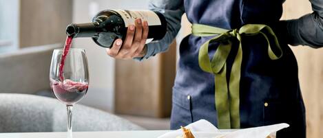 A person pouring red wine into a glass, standing next to a plate with food.