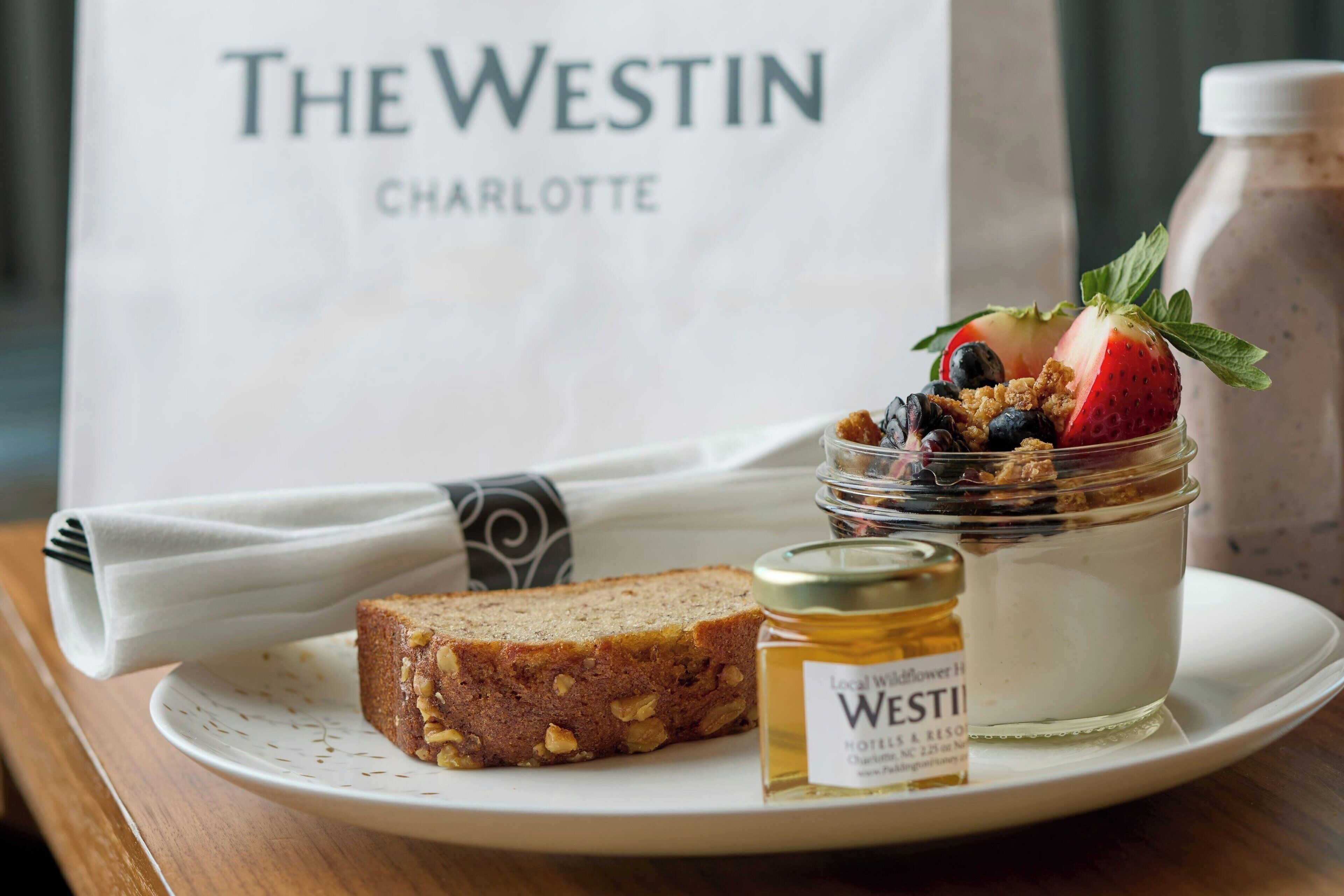 A breakfast plate with a slice of bread, a yogurt parfait with berries and granola, and a honey jar labeled "Westin Charlotte".