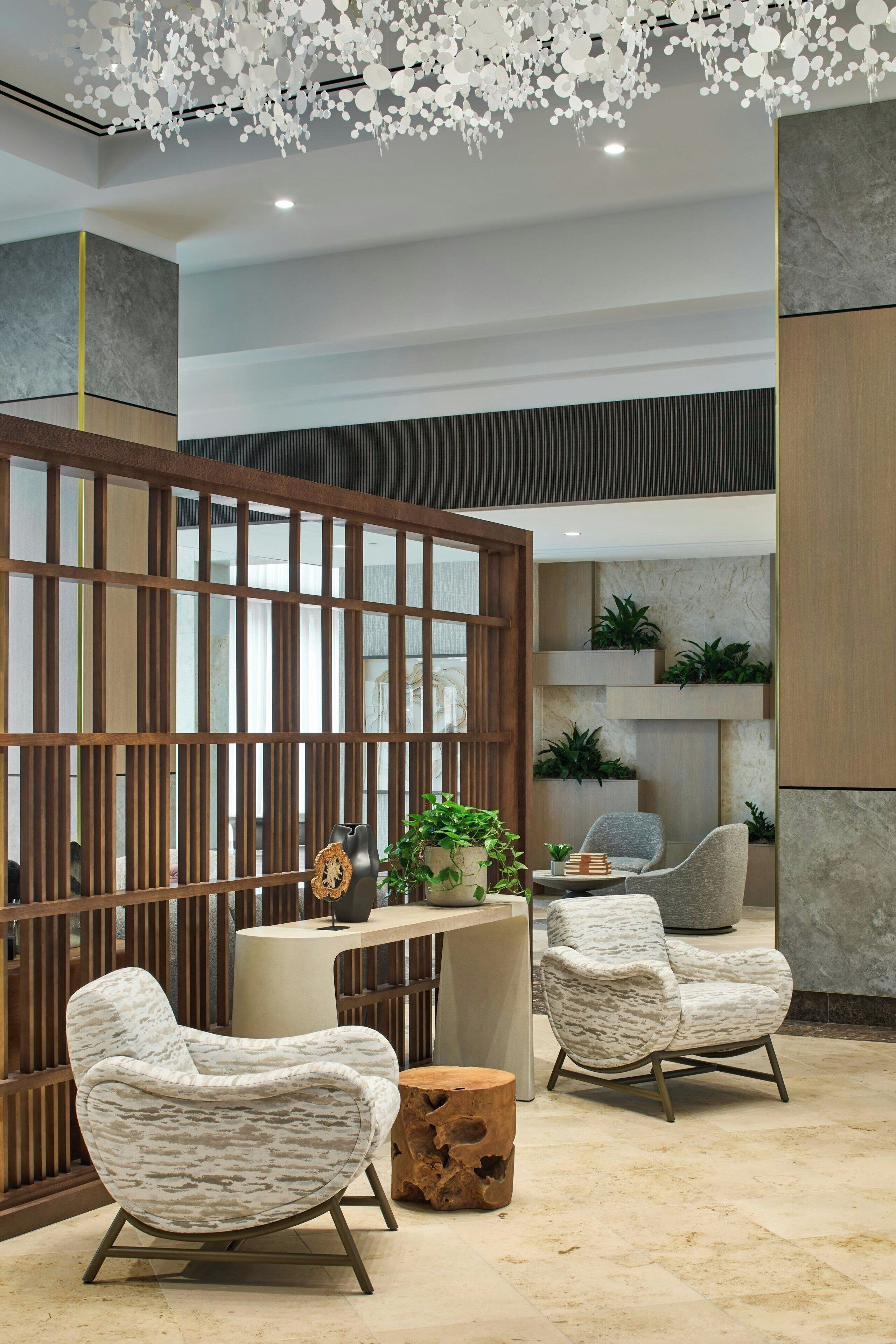 A modern interior with a wooden partition, two upholstered chairs, a round wooden table, and a decorative ceiling.