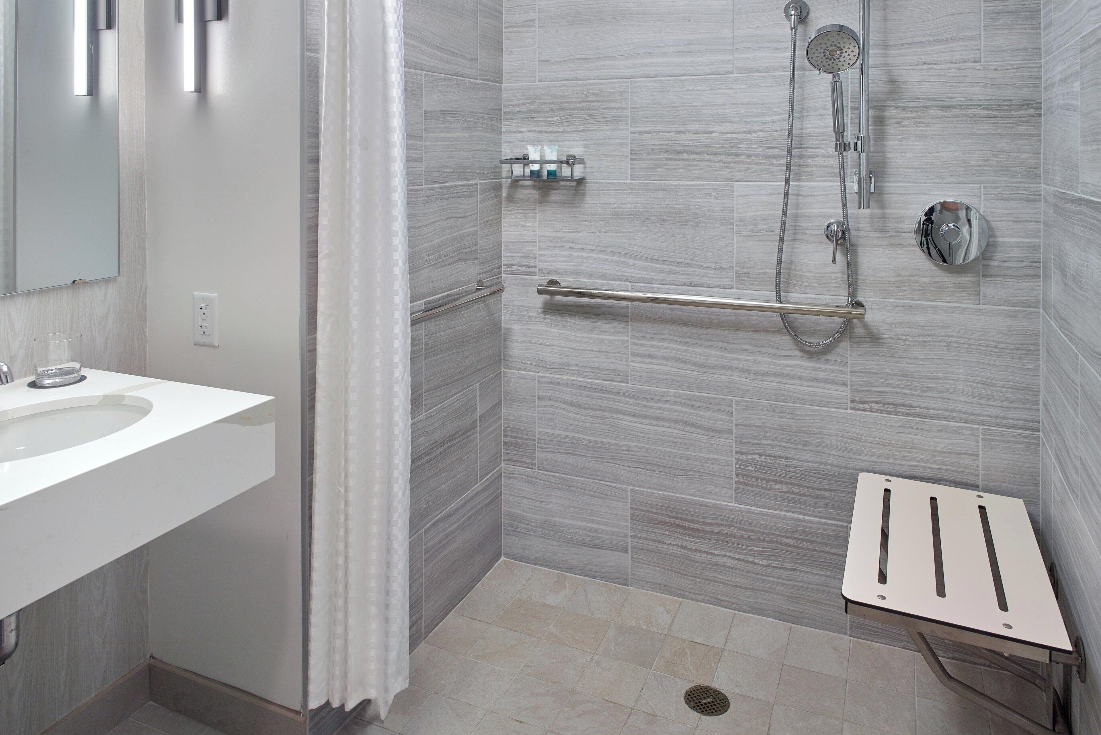 A modern bathroom with a white sink, a shower with a handheld showerhead, and a grab bar.