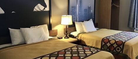 Habitación de hotel con dos camas, una mesita de noche con lámpara, armario para abrigos y un cuadro con una vista urbana.