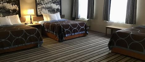 A hotel room with two beds, a large window with curtains, a carpeted floor, and two framed pictures on the wall.