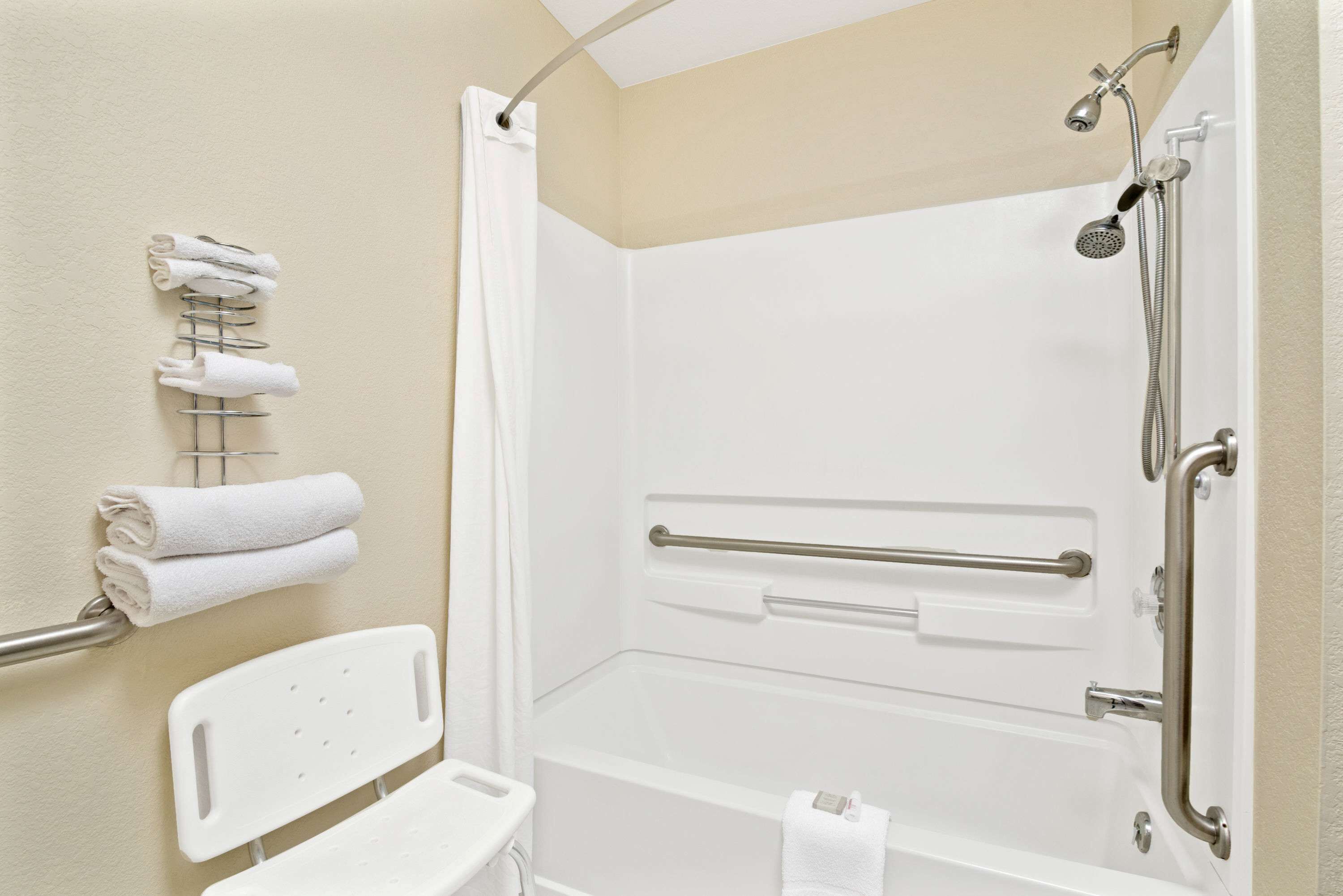 A bathroom with a shower, grab bars, and a white towel rack.