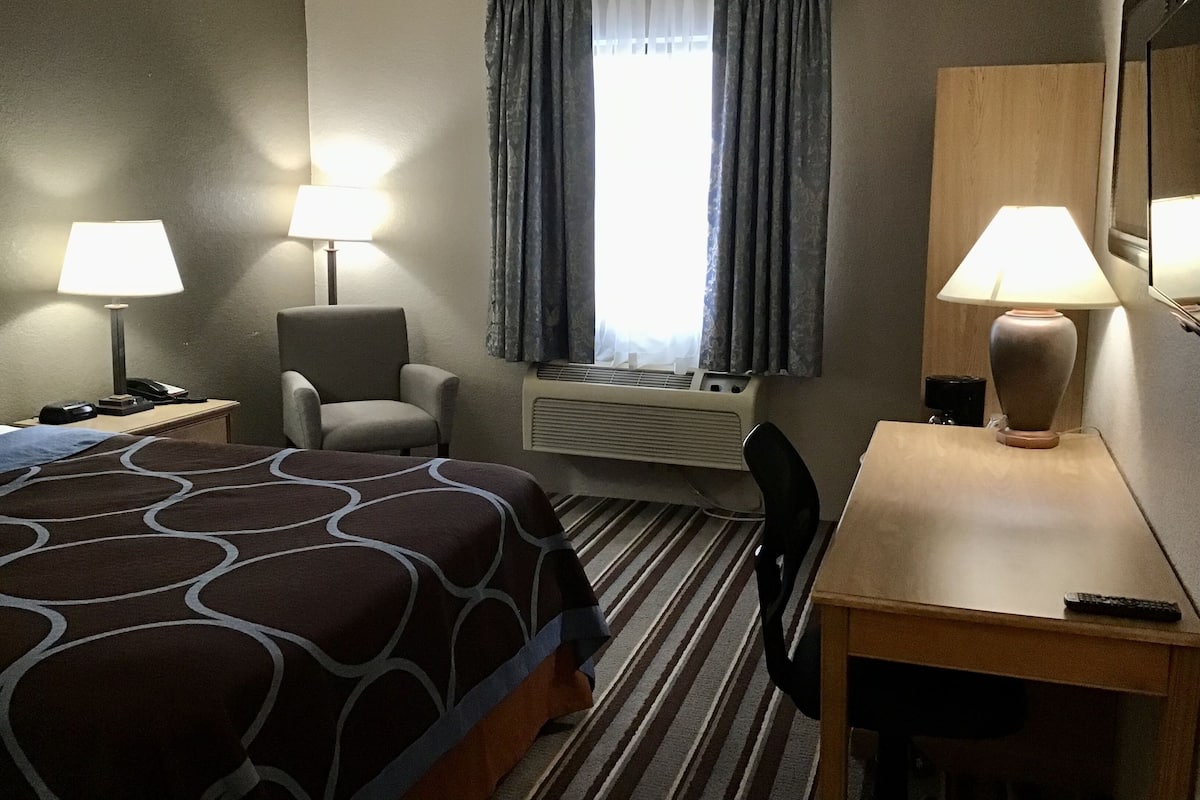 A hotel room with a bed, a desk, a chair, a lamp, a telephone, and a window with curtains.