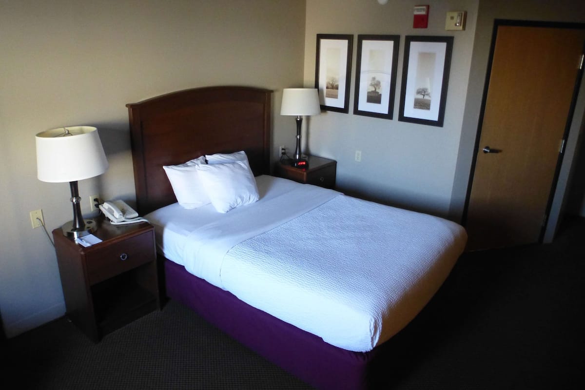 A hotel room with a bed, two bedside tables with lamps, a telephone, and framed pictures on the wall.