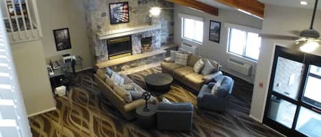 A spacious living room with a stone fireplace, comfortable seating, and large windows.