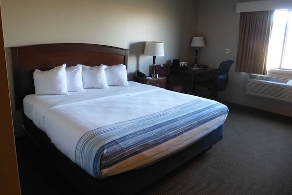 A hotel room with a large bed, a desk, a chair, and an air conditioning unit. - AmericInn by Wyndham Mitchell (Mitchell)