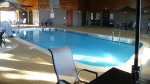 Una piscina interior con sillas de descanso y sombrillas, techo de madera y paredes de baldosas.