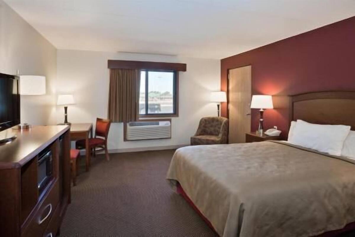 A hotel room with a bed, a desk, a chair, a TV, and a window.