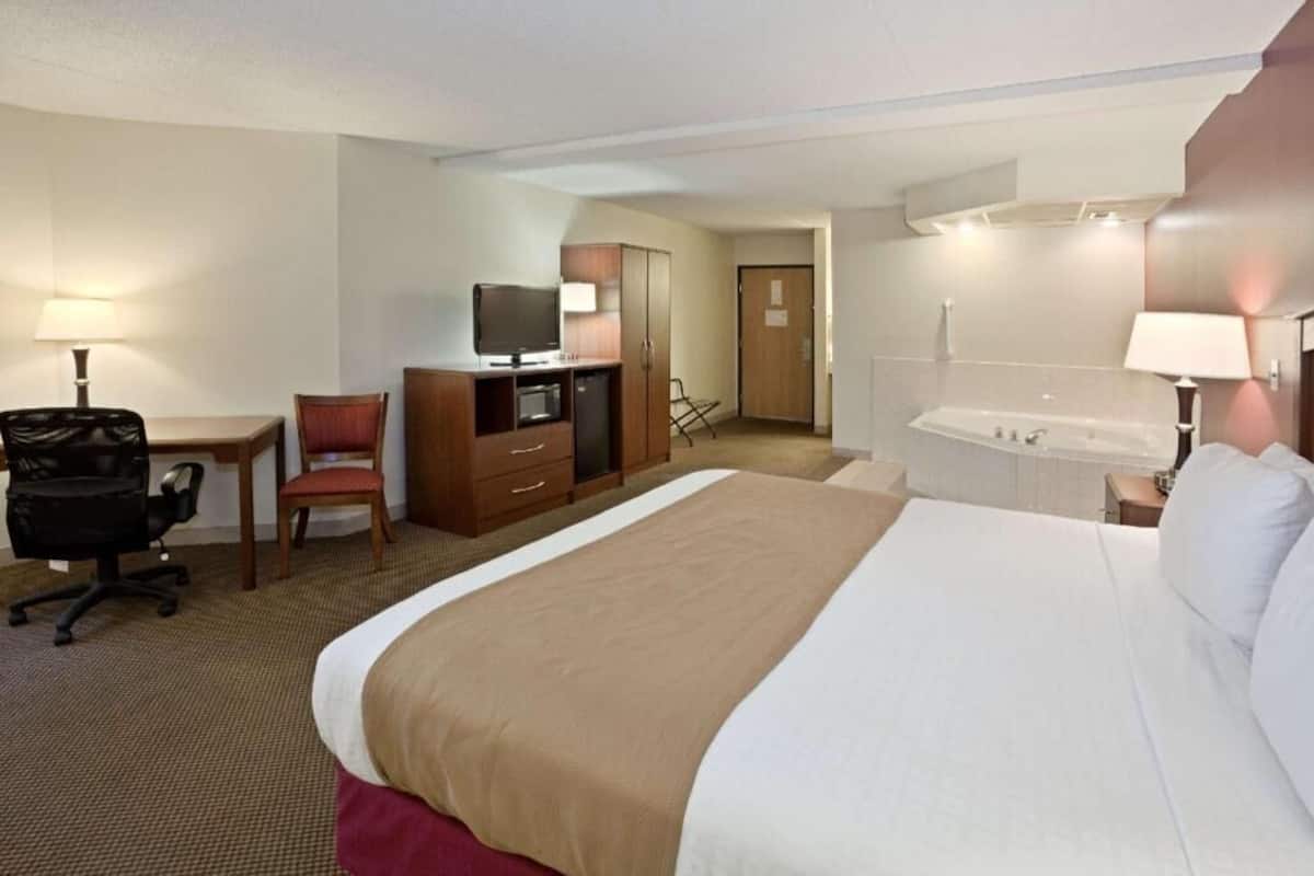 A hotel room with a bed, desk, chair, TV, minibar, and a bathroom with a bathtub.