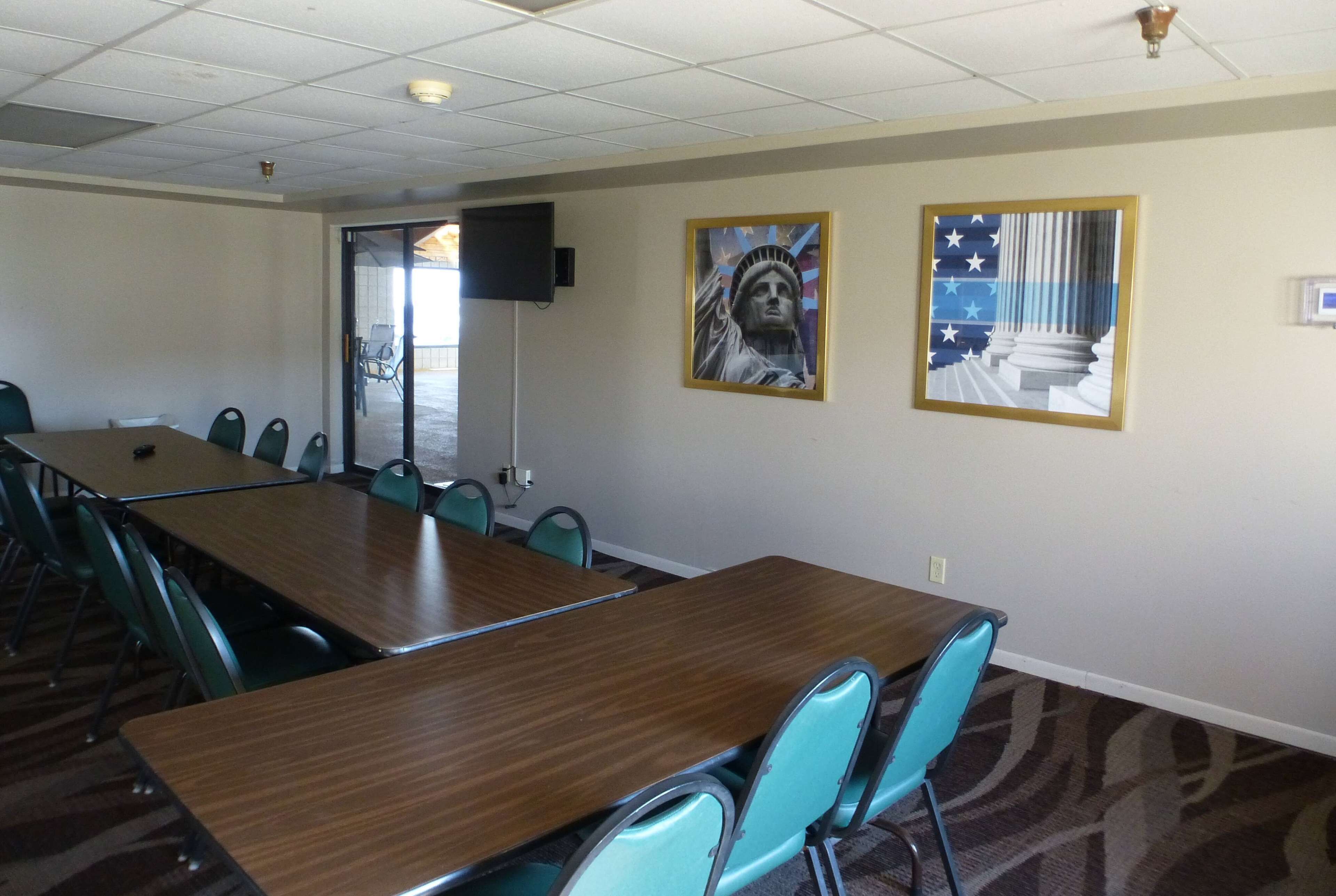 Ein Konferenzraum mit einem langen Tisch, Stühlen, einer Projektionsleinwand und zwei gerahmten Kunstwerken an der Wand.