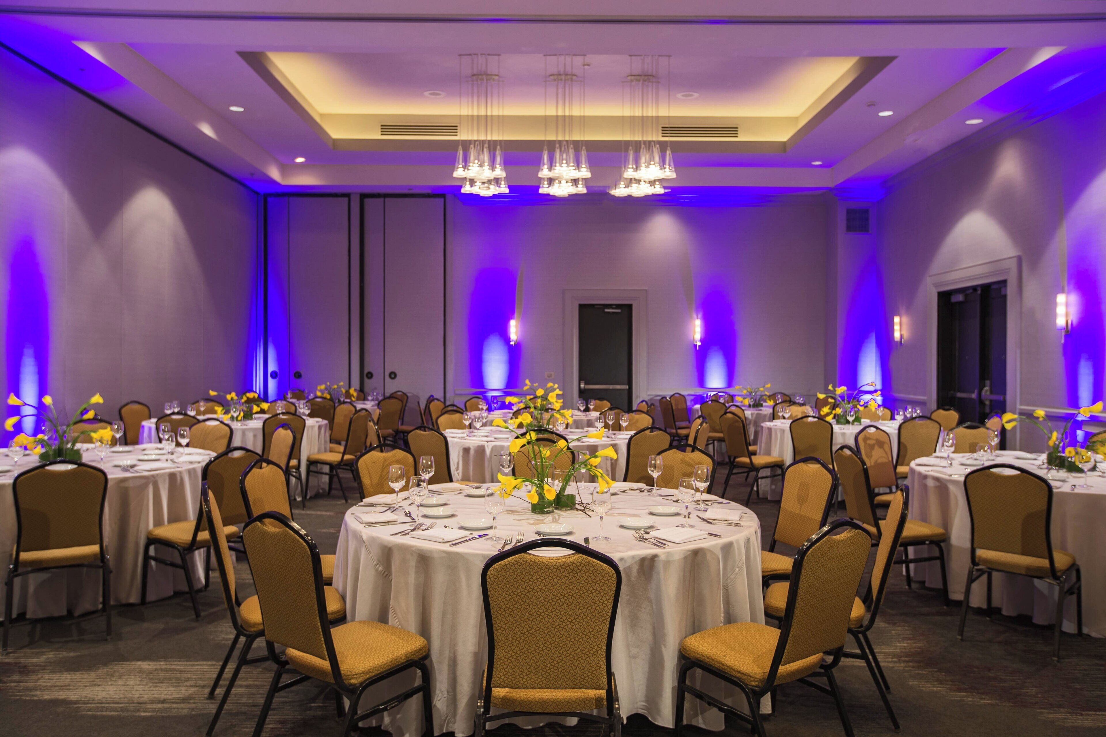 A banquet hall with round tables, chairs, and floral centerpieces.