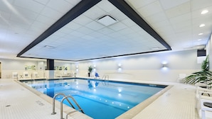 Una piscina interior con suelo de baldosas, una escalera y luces fijadas a la pared.