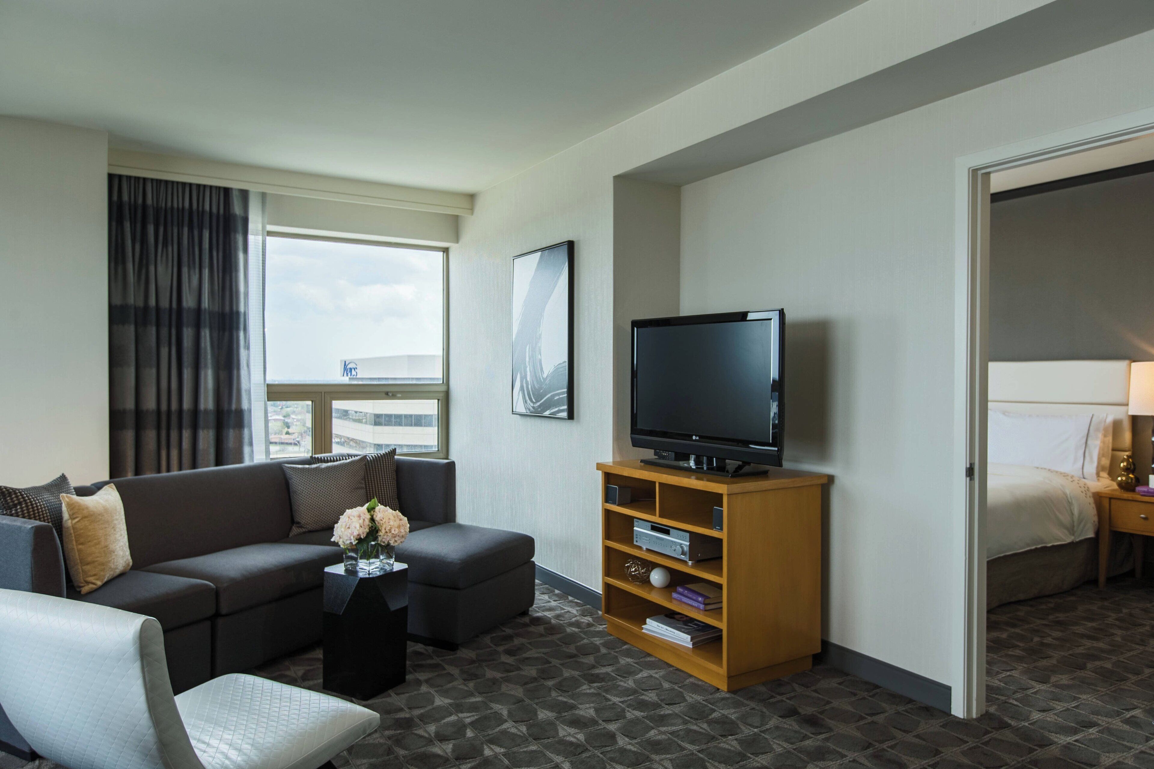 Una habitación de hotel con sofá, reposapiés, mueble para televisión y cama.