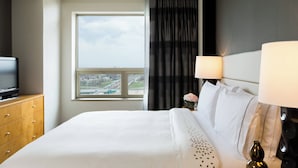 Una habitación de hotel con cama, televisión en una cómoda de madera, ventana con vista a la ciudad y lámpara en la mesita de noche.