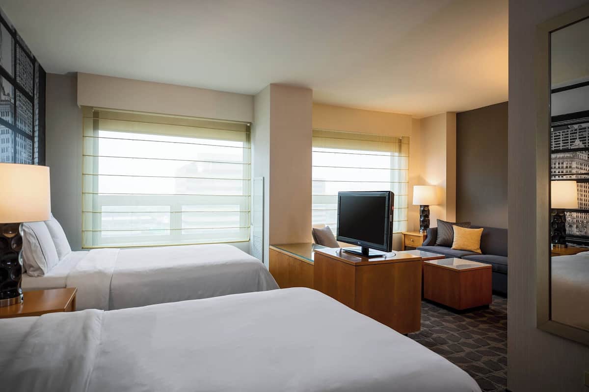 A hotel room with two beds, a desk, a television, and a sofa.