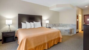 A hotel room with a large bed, two bedside tables with lamps, a built-in headboard, a marble-tiled bathroom with a bathtub, and a dark-colored wardrobe. - Best Western Carowinds (Fort Mill)