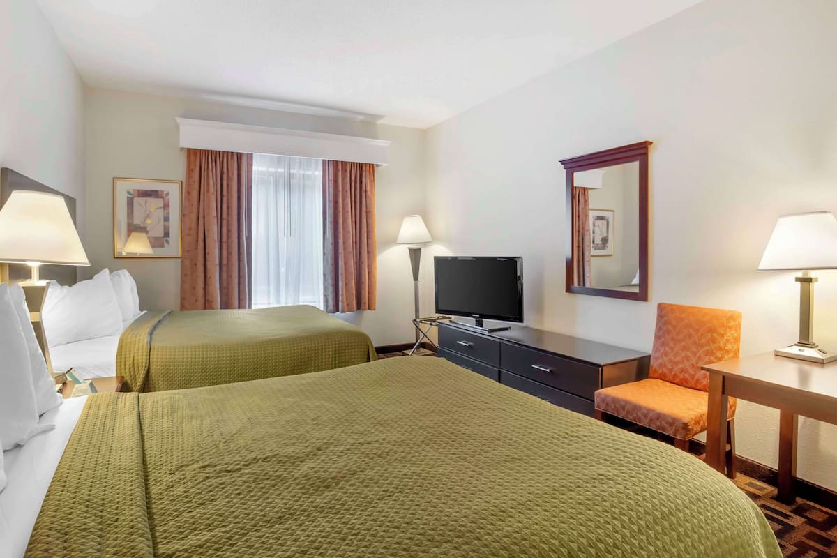 A hotel room with two beds, a TV, a desk, a chair, and a window with curtains.