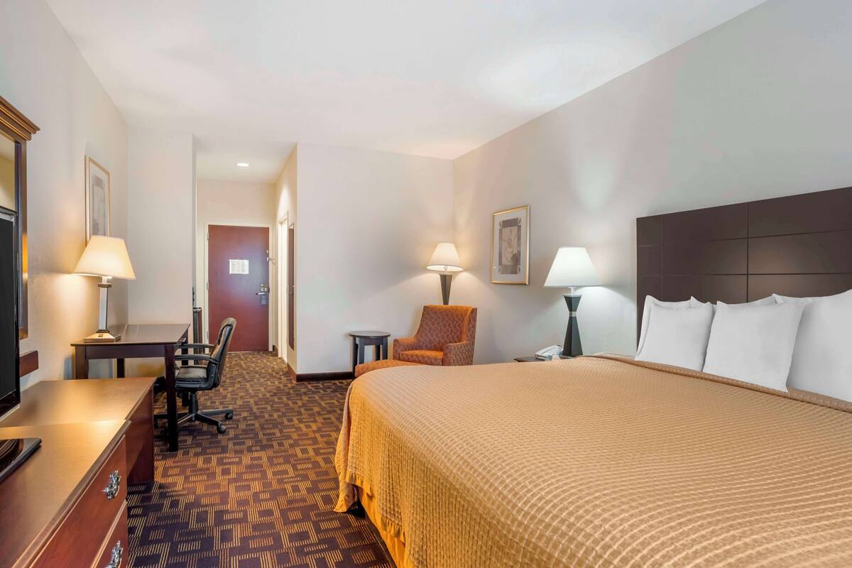 A hotel room with a bed, desk, chair, and lamps.