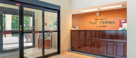 A hotel entrance with a reception desk, emergency exit doors, and a tiled floor.