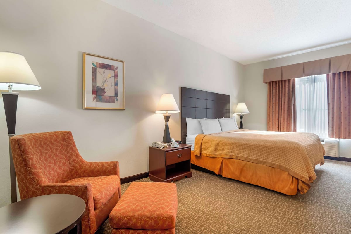 A hotel room with a bed, a chair, a nightstand, a lamp, and a painting on the wall.