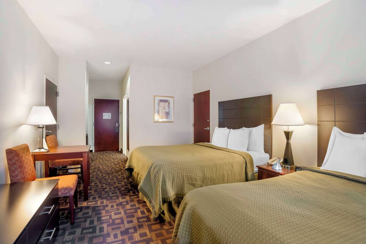 A hotel room with two beds, a desk, a chair, and a small table.