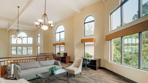 A spacious living area with a sofa, armchair, and coffee table, large windows, and a wooden ceiling. - Best Western Carowinds (Fort Mill)