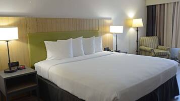 A neatly made bed with white linens, a green headboard, and two bedside lamps.