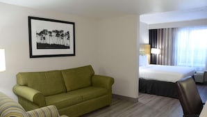 A hotel room with a green sofa, a striped sofa, a bed, a desk, and a framed picture on the wall. - Country Inn & Suites by Radisson, Buford at Mall of Georgia, GA (Buford)