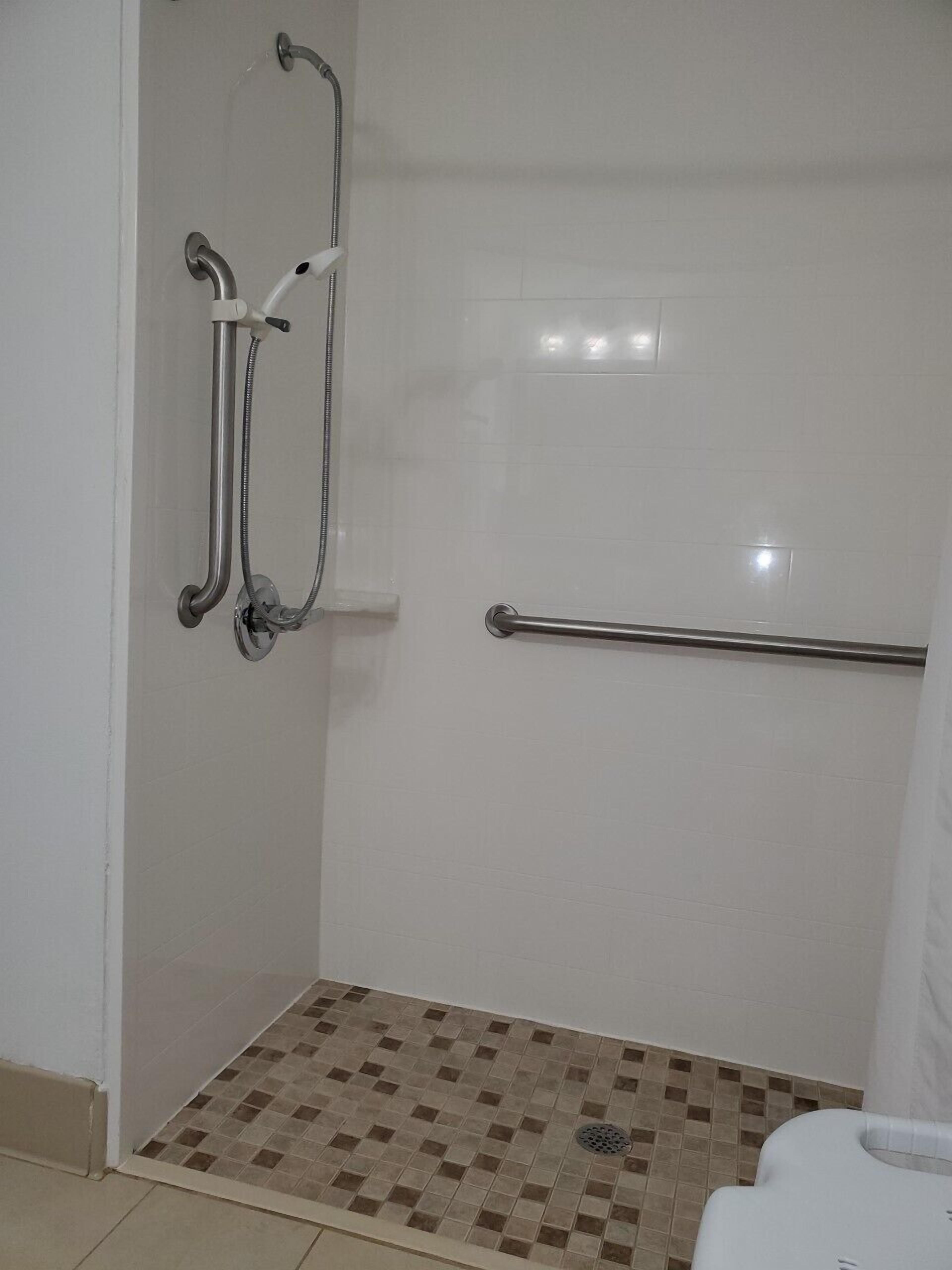 A bathroom with a shower area, a grab bar, and a tiled floor.