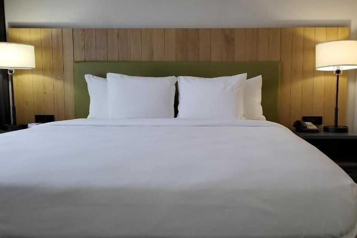 Una cama grande con ropa blanca, dos lámparas de noche y un cabecero de madera.